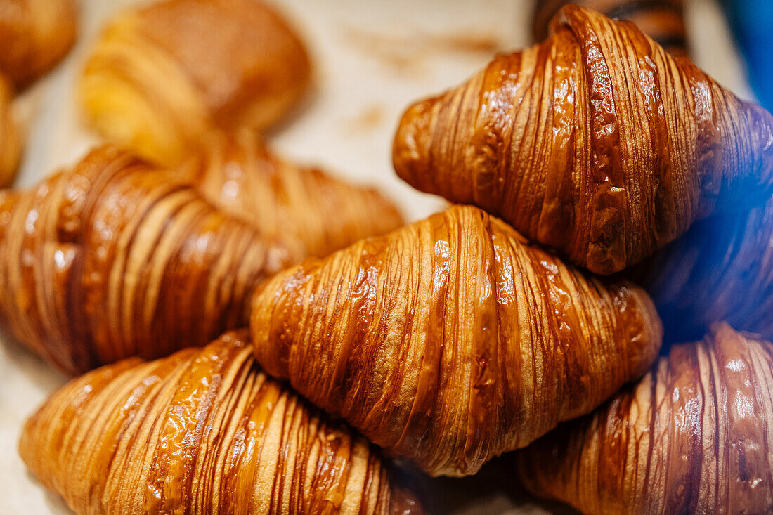 Heap of tasty crispy brown croissants placed on parchment in showcase of modern light confectionery with pastry on blurred background