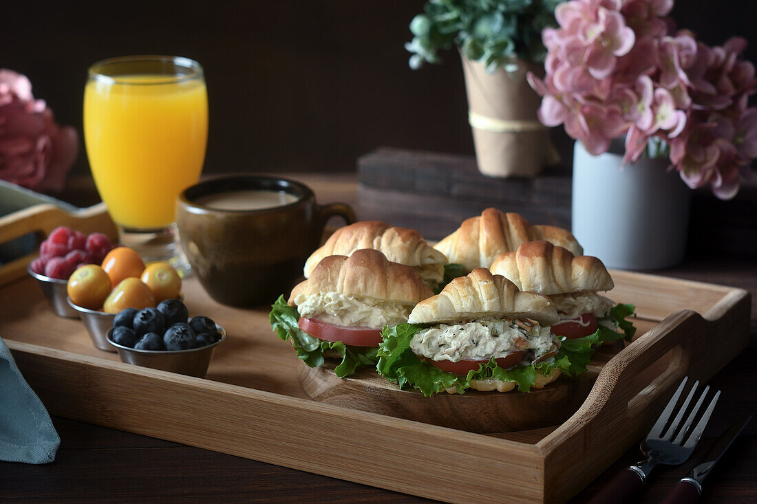 Delicious croissant sandwiches with vegetables served on tray with cappuccino and orange juice prepared for French breakfast and placed on wooden table