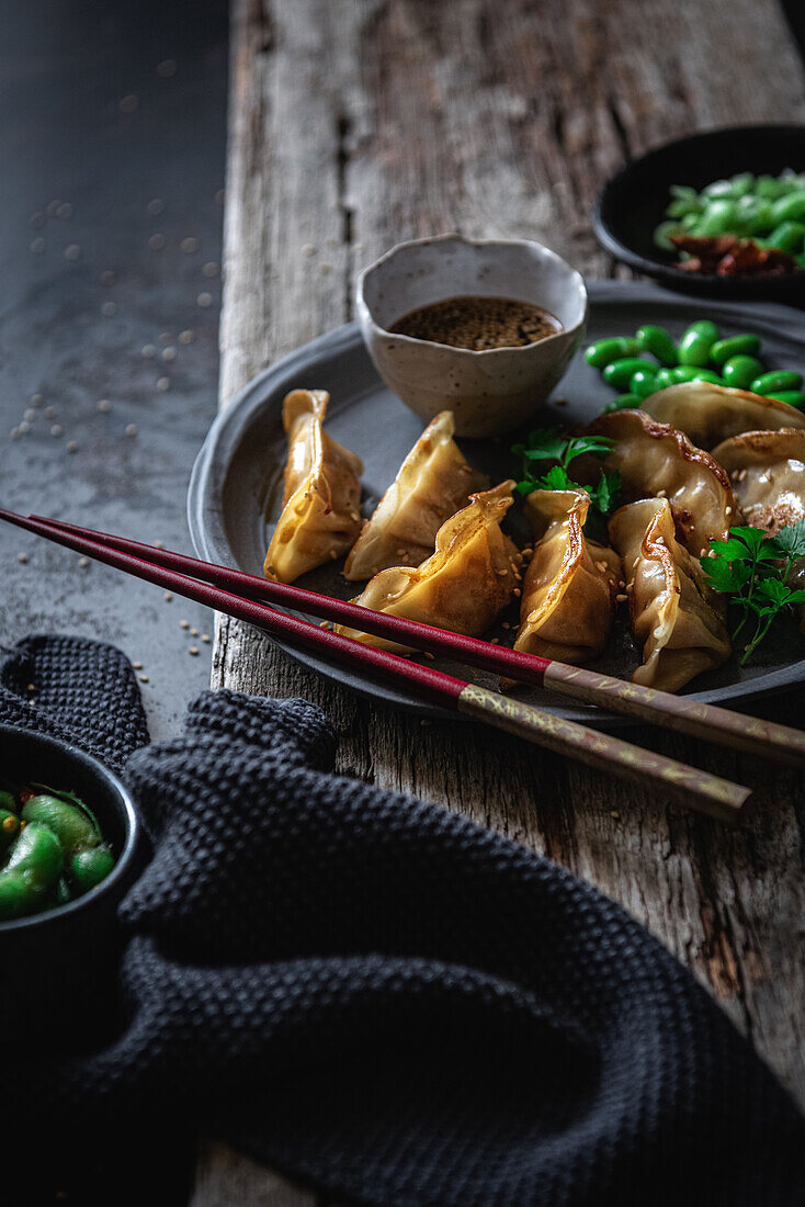 Gyozas mit grünen Bohnen und Sojasauce mit Sesam werden mit Stäbchen neben Schalen mit Gewürzen und Erbsenschoten platziert