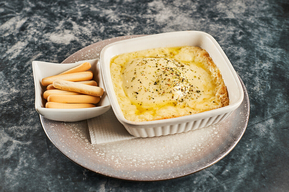 Pfanne mit köstlichem Provoleta-Käse und Schale mit Löffelbiskuits auf Teller auf grauem Marmortisch