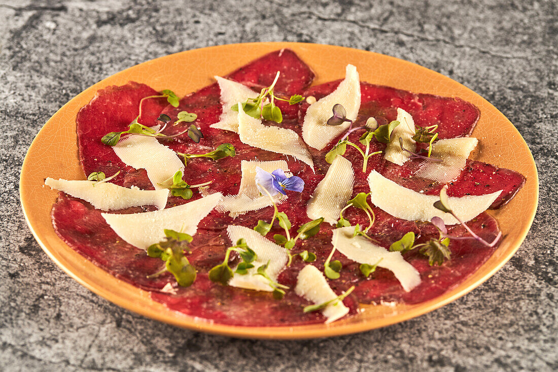 From above slices of veal with lemon and oil with black pepper garnished with sprouts and slices of parmesan cheese and served on plate on gray marble table in restaurant