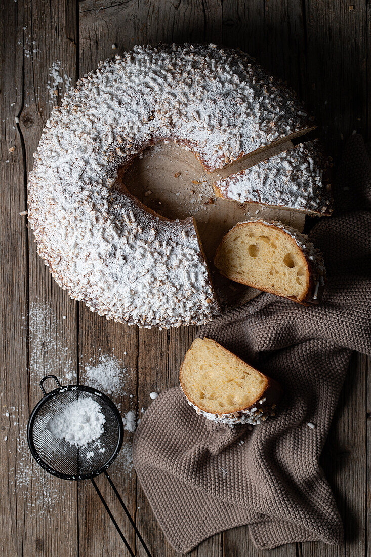 Top view of appetizing cut of king's cake dusted with icing sugar and placed on wooden table against towel