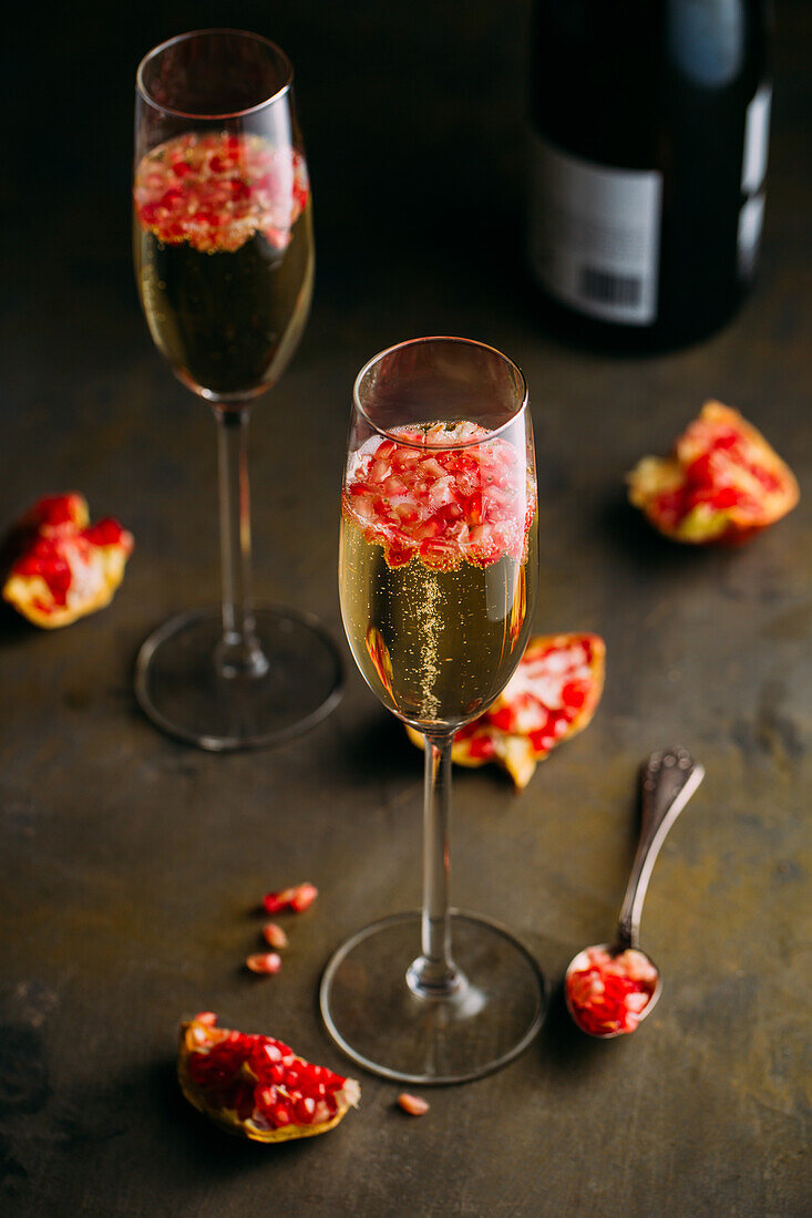 Stillleben eines Champagnercocktails mit Granatapfel auf einer rustikalen Oberfläche