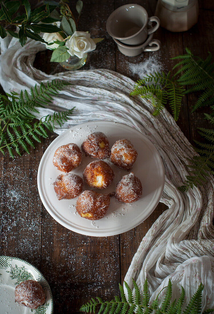 From above homemade custard cream fritters covered with sugar on rustic wooden table with table cloth and leafs decoration