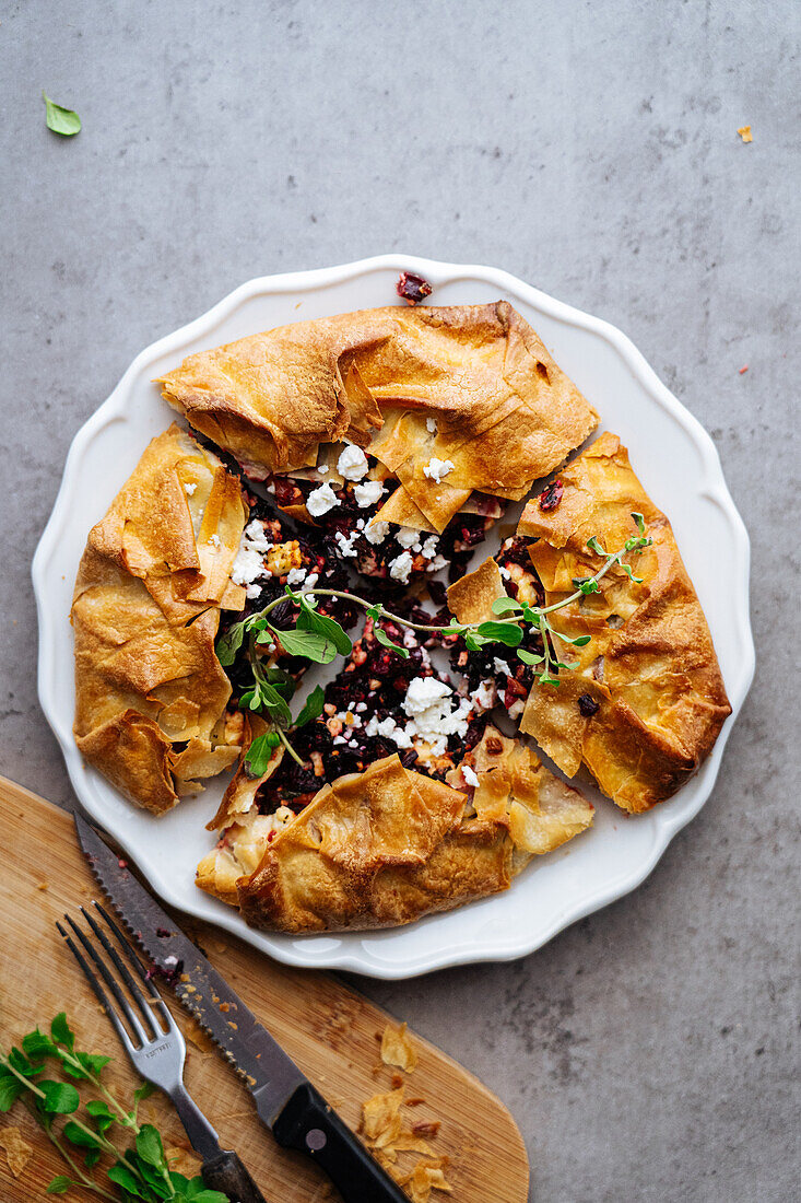 Top view of baked cut pie with beetroot and feta cheese on ceramic plate with knife on gray background in kitchen