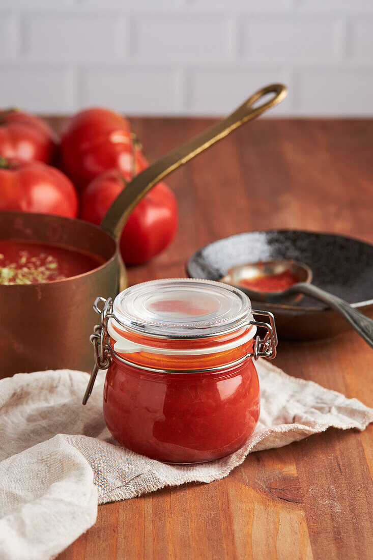 Glass jar with fresh tomato sauce placed on woven mat in kitchen at home