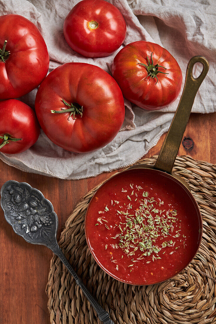 Draufsicht auf eine Pfanne mit köstlicher hausgemachter Tomatensauce und Oregano auf einer gewebten Matte auf einem Holztisch in der Küche