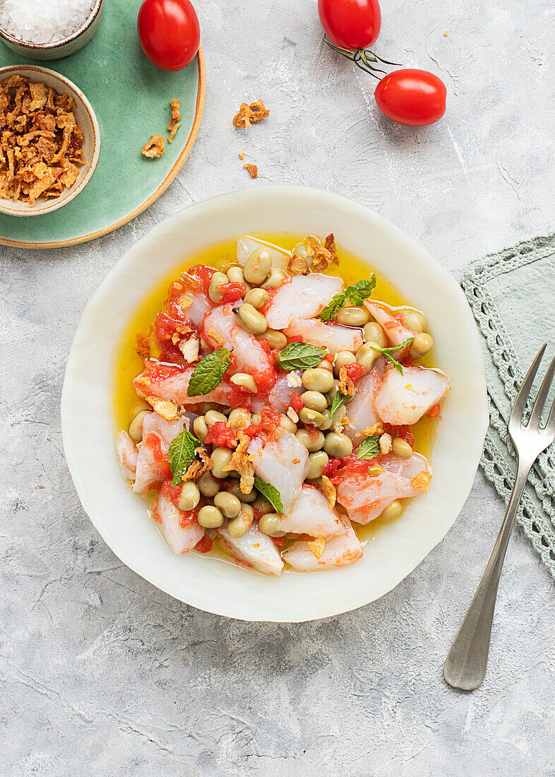 Tomaten- und Kabeljausalat mit reichlich Olivenöl in einem tiefen Teller mit einer Gabel und einer Schale mit gebratenen Zwiebeln