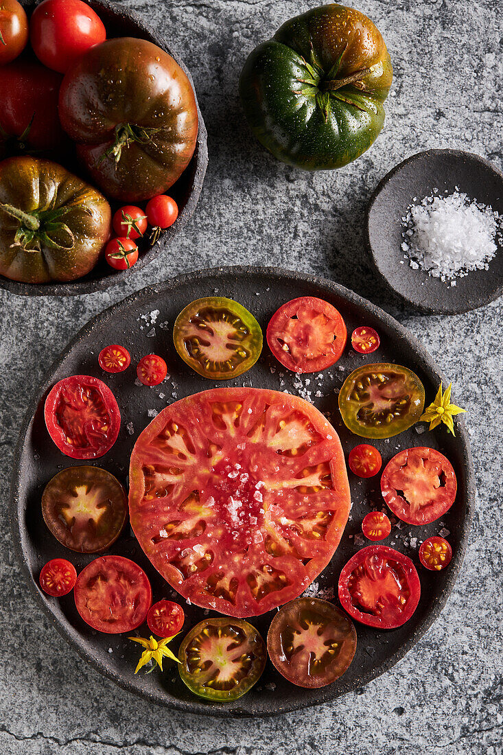 Top view of delicious sliced tomatoes in cast iron plate near sea salt and jug of olive oil on concrete table