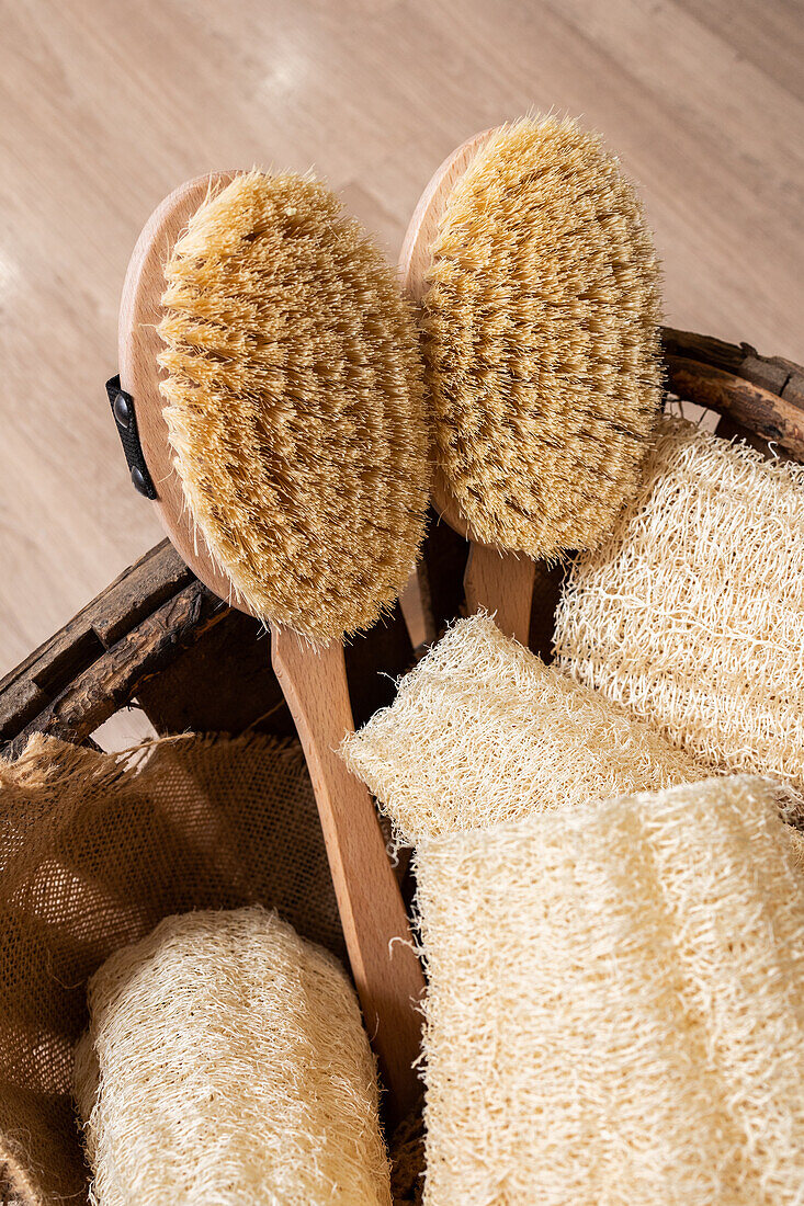 Top view of wooden basket placed on floor filled with brushes and zero waste natural luffa sponges