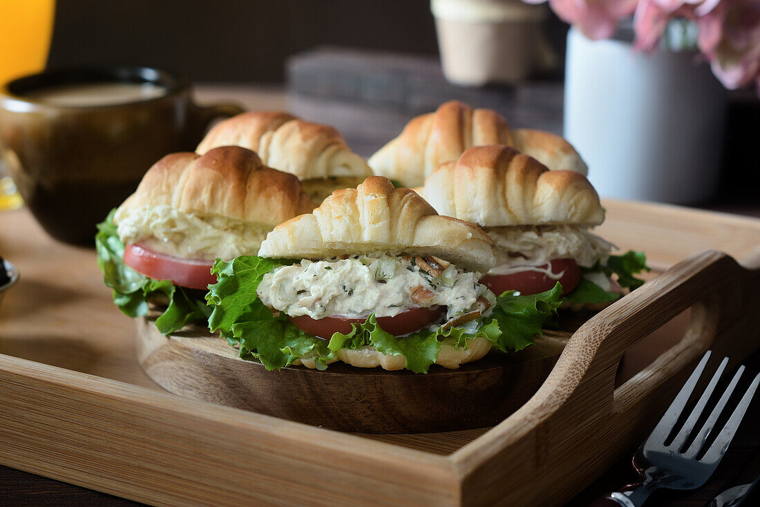 Delicious croissant sandwiches with vegetables served on tray with cappuccino and orange juice prepared for French breakfast and placed on wooden table