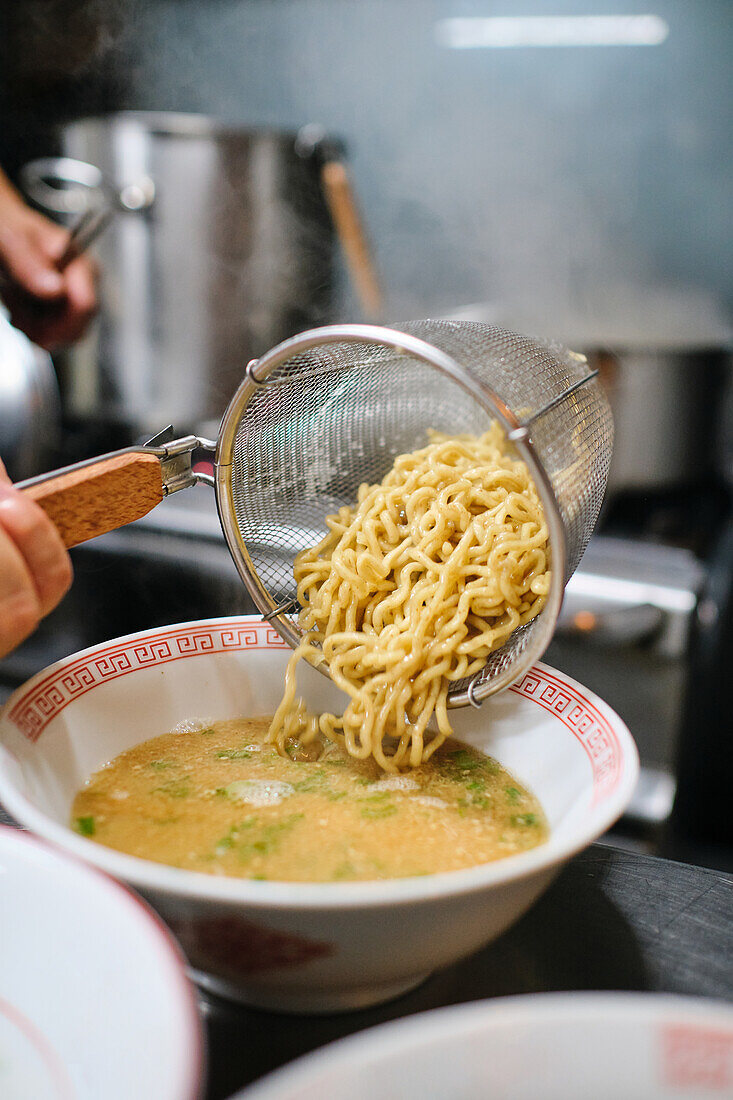 Stock photo of unrecognized chef in japanese restaurant serving noddles soup.