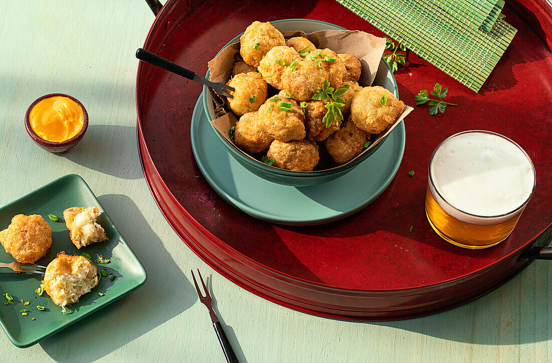 From above traditional codfish fritters server on tray with fresh herbs and glass of beer on green background