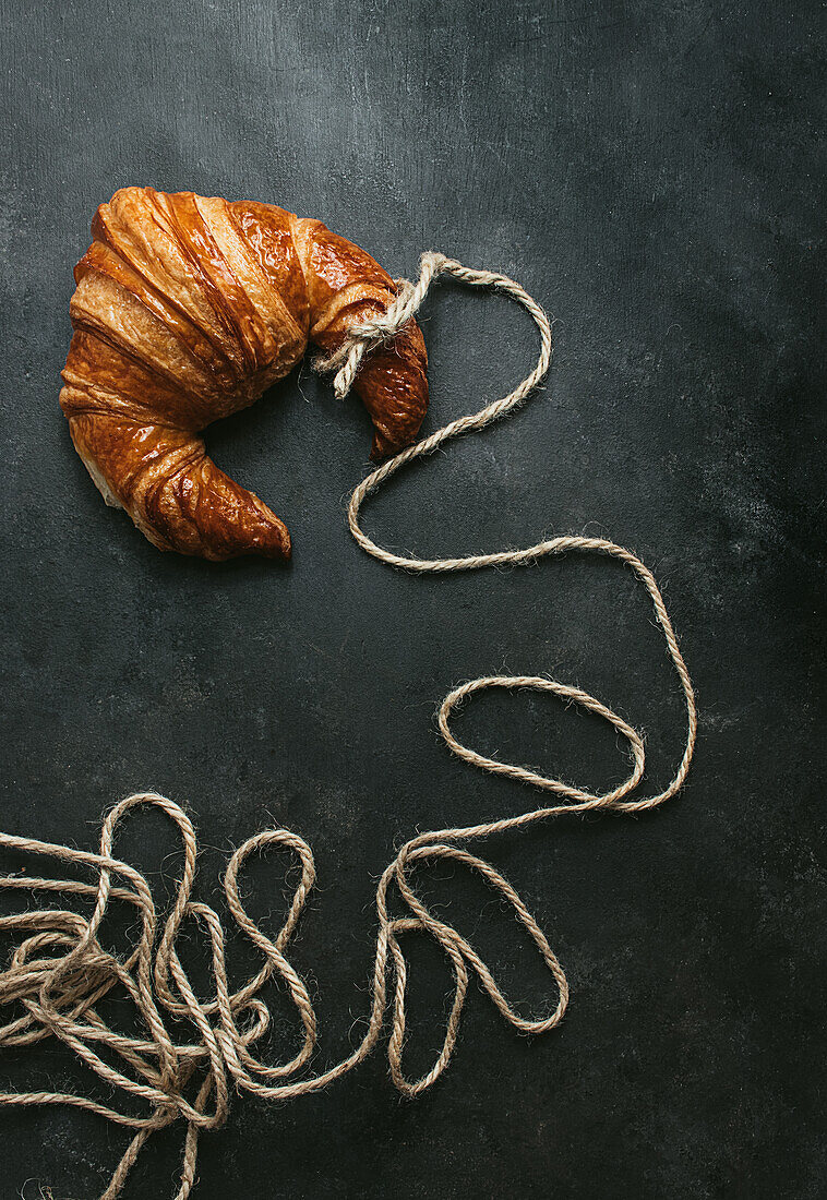 Von oben köstliches frisch gebackenes traditionelles Croissant mit Seil umwickelt auf schwarzem Hintergrund