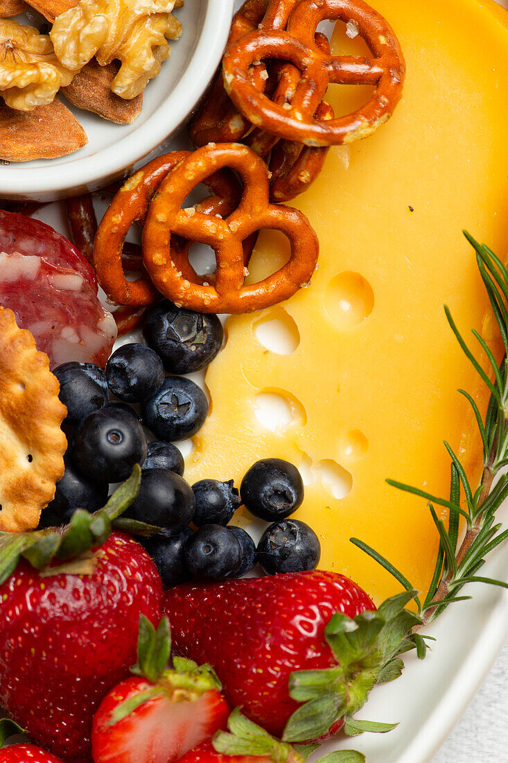 Draufsicht auf leckere Charcuterieplatte mit verschiedenen Käsesorten und Nüssen, serviert mit reifen Erdbeeren auf Tisch in heller Küche