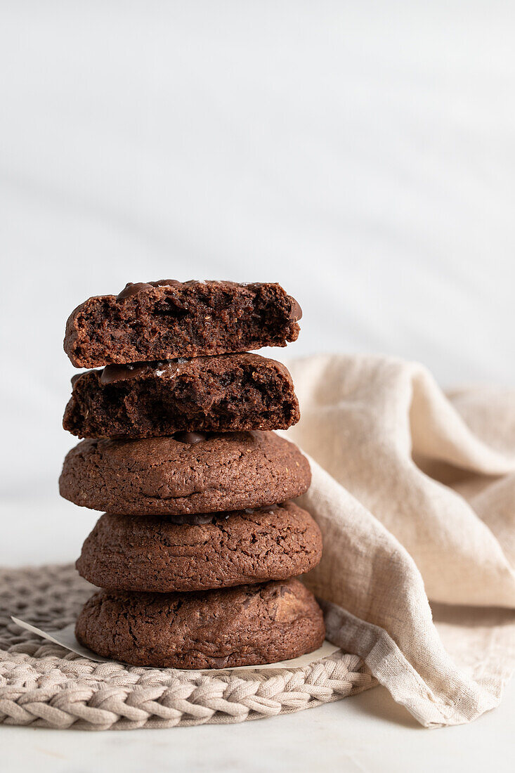 Pile of chocolate rye cookies placed on wicker plate near napkin on white background