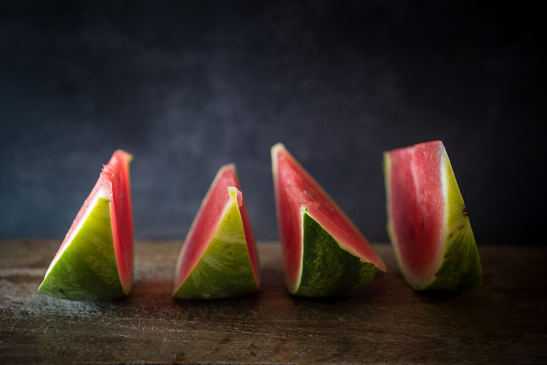 Delicious ripe watermelon slices with juicy pulp in row on wooden surface on blurred background
