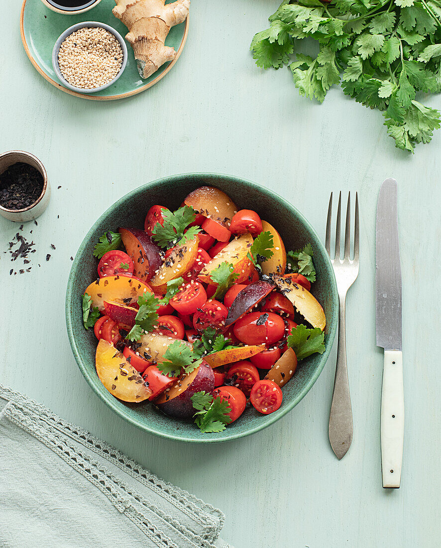 Draufsicht auf einen rohen Tomatensalat mit Obst auf einem Tisch mit grünem Tischtuch, umgeben von gesunden Zutaten