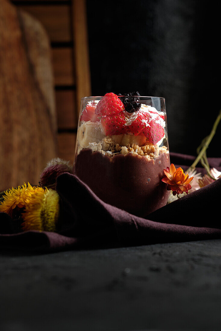 Appetitanregende Smoothie-Schale mit Granola, Erdbeeren und Blaubeeren auf einem Tisch in der Nähe verschiedener Wildblumen