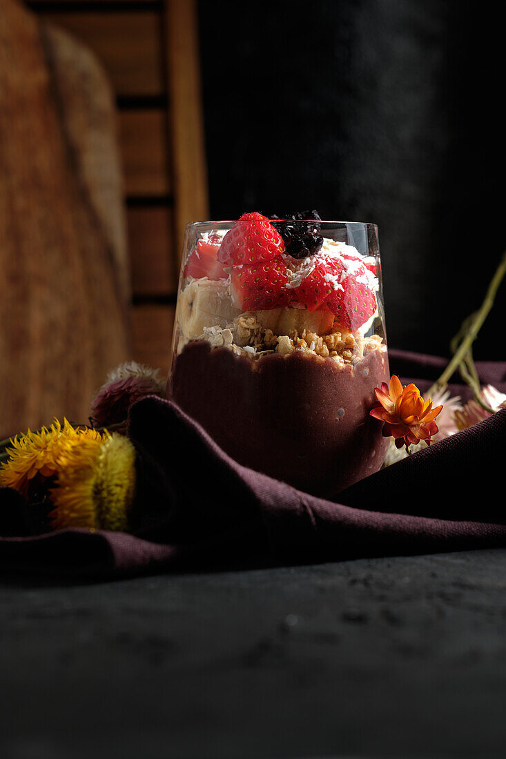 Appetizing smoothie bowl with granola strawberries and blueberries placed on table near various wildflowers