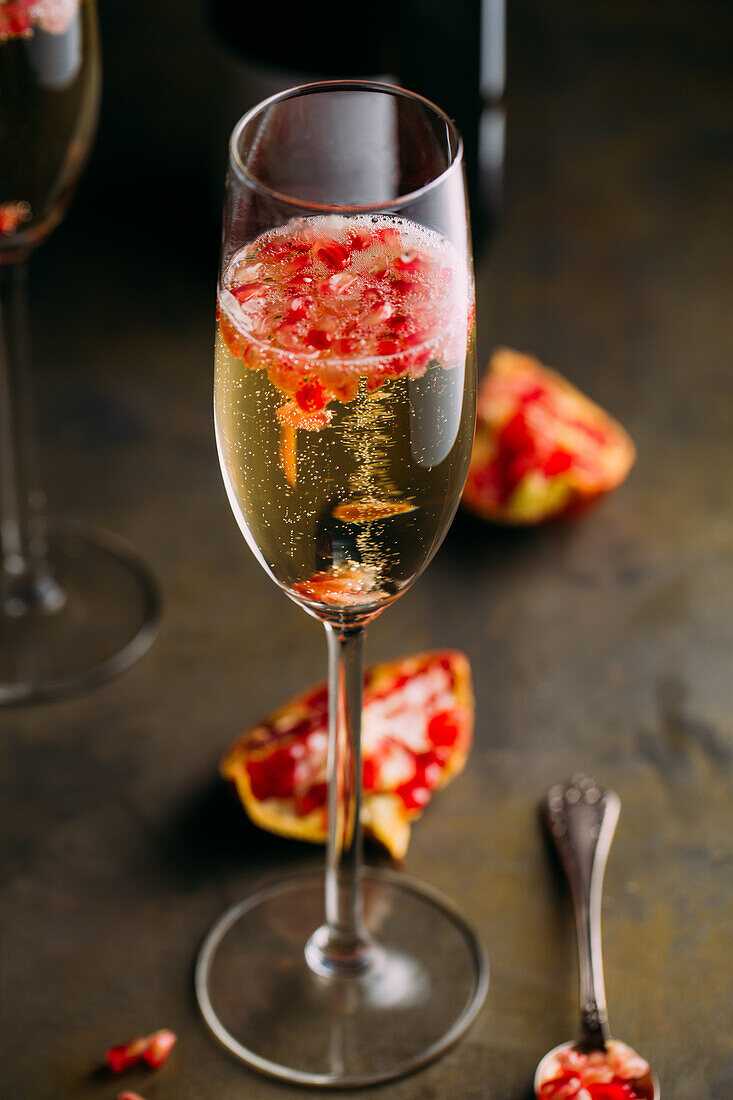 Stillleben eines Champagnercocktails mit Granatapfel auf einer rustikalen Oberfläche