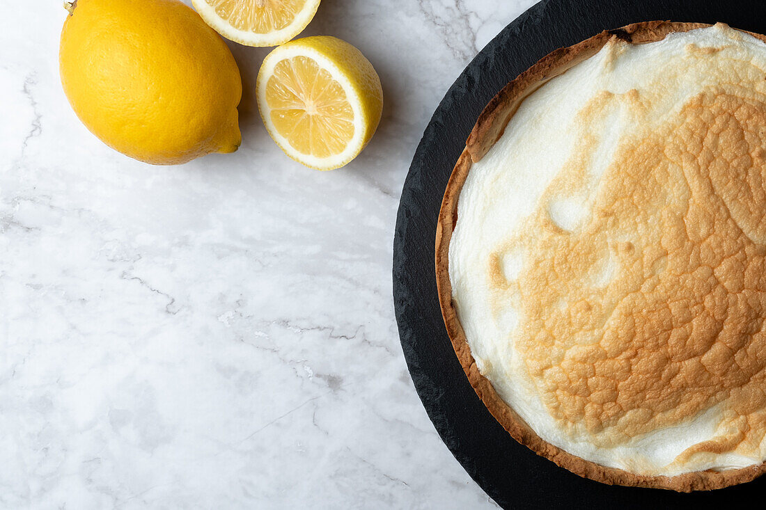 Draufsicht auf eine appetitliche Baisertorte, die auf einem Marmortisch mit frischen Zitronen in der Küche serviert wird