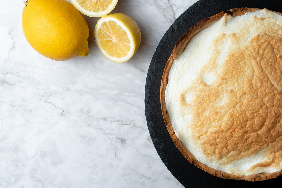 Top view of appetizing meringue pie served on marble table with fresh lemons in kitchen