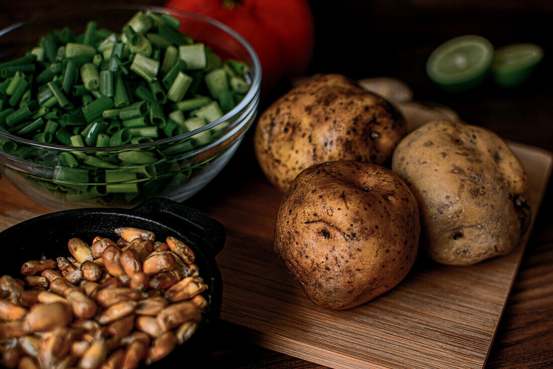 High angle of raw potatoes and chopped spring onion placed on wooden cutting board near bowl with grains prepared for cooking chicken broth