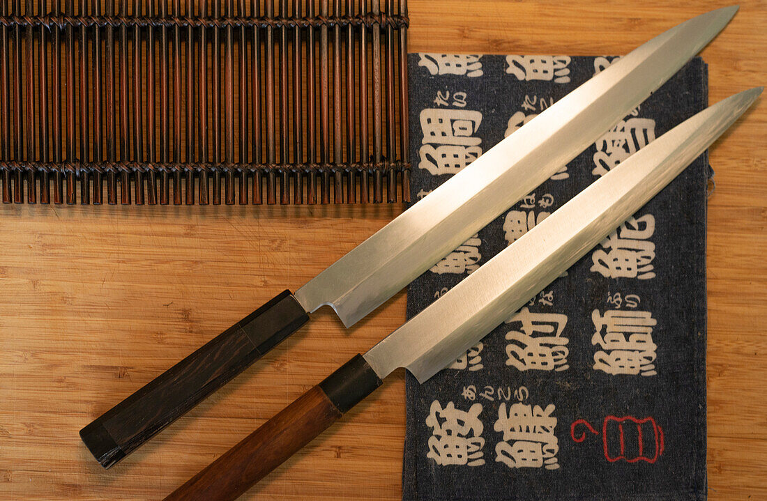 Draufsicht auf scharfe Messer und Sushi-Matte auf Holztisch in asiatischem Restaurant