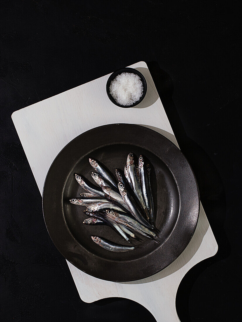 Top view of raw small fishes in plate on white board on black background