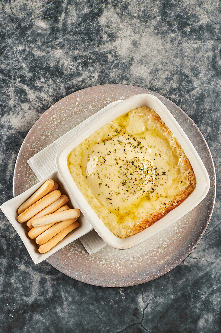 Draufsicht auf eine Pfanne mit leckerem Provoleta-Käse und eine Schale mit Löffelbiskuits auf einem Teller auf einem grauen Marmortisch