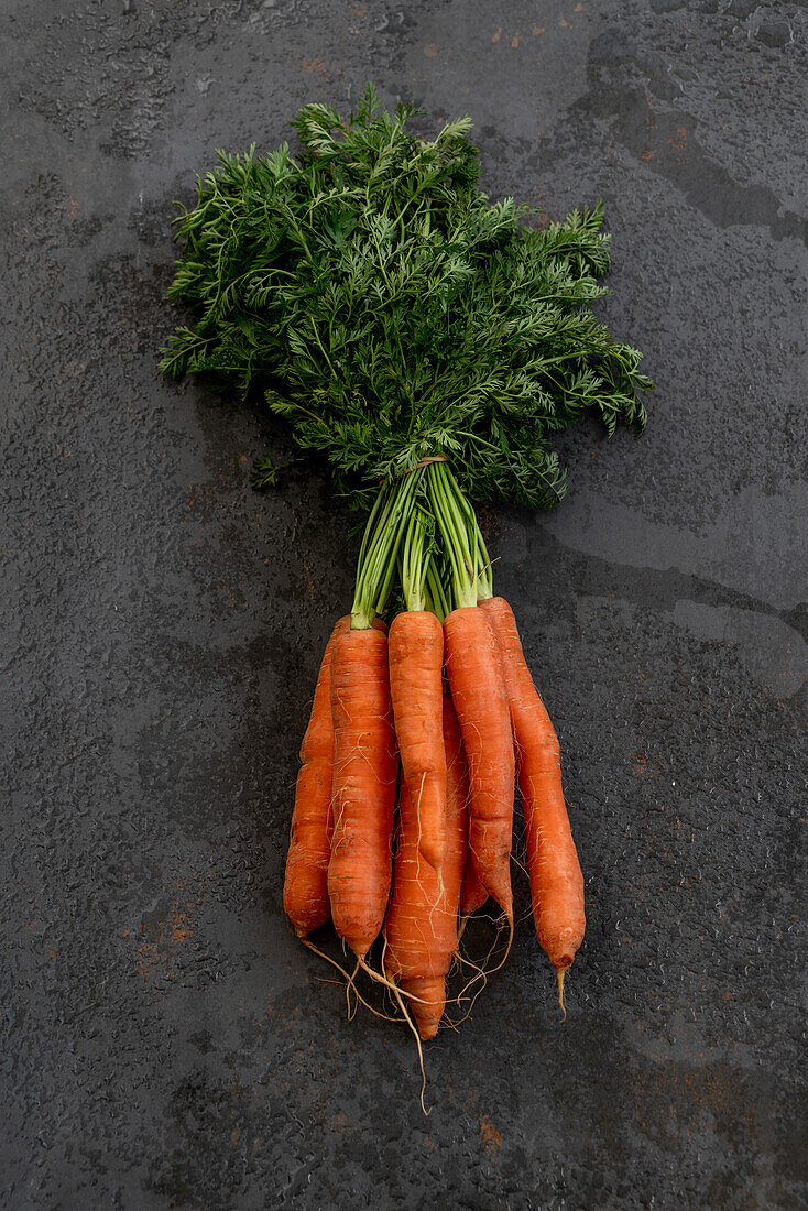 From above of bunch of ripe carrots placed on black shabby background in studio