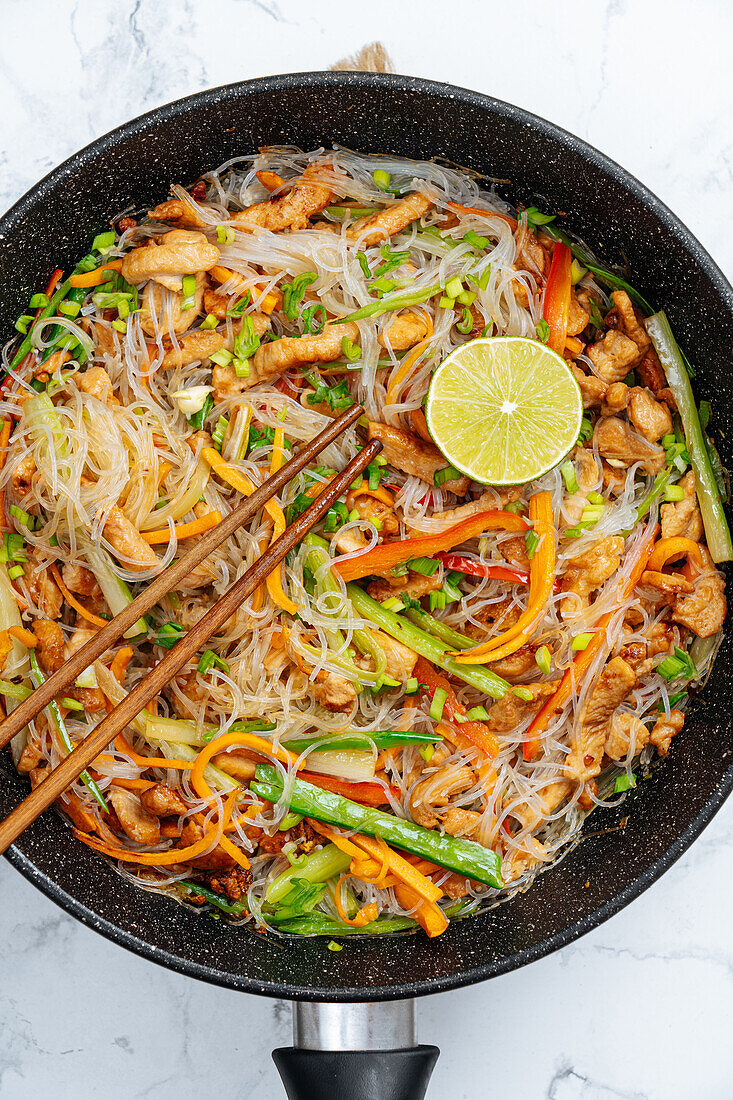 From above chopsticks on tasty stir fry rice noodles with vegetables served in frying pan