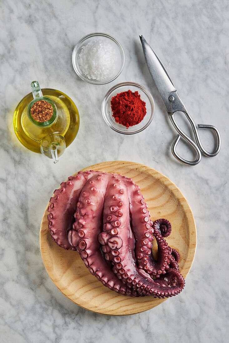 Top view of fresh raw octopus placed on round wooden plate near metal scissors spices and oil