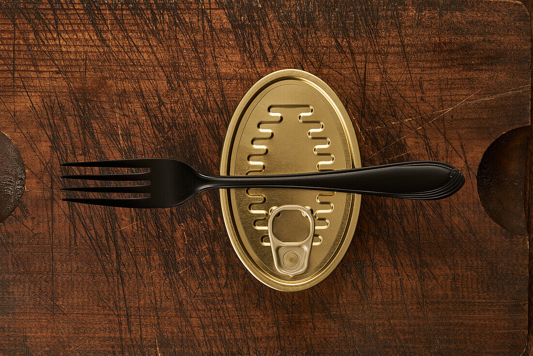 From above scratched chopping board with fork and sealed can with preserved food on rustic lumber table