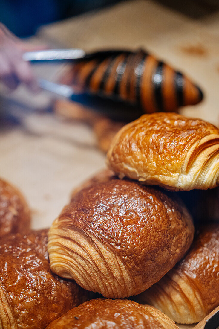 Heap of tasty crispy brown chocolatine placed on parchment in showcase of modern light confectionery with pastry on blurred background