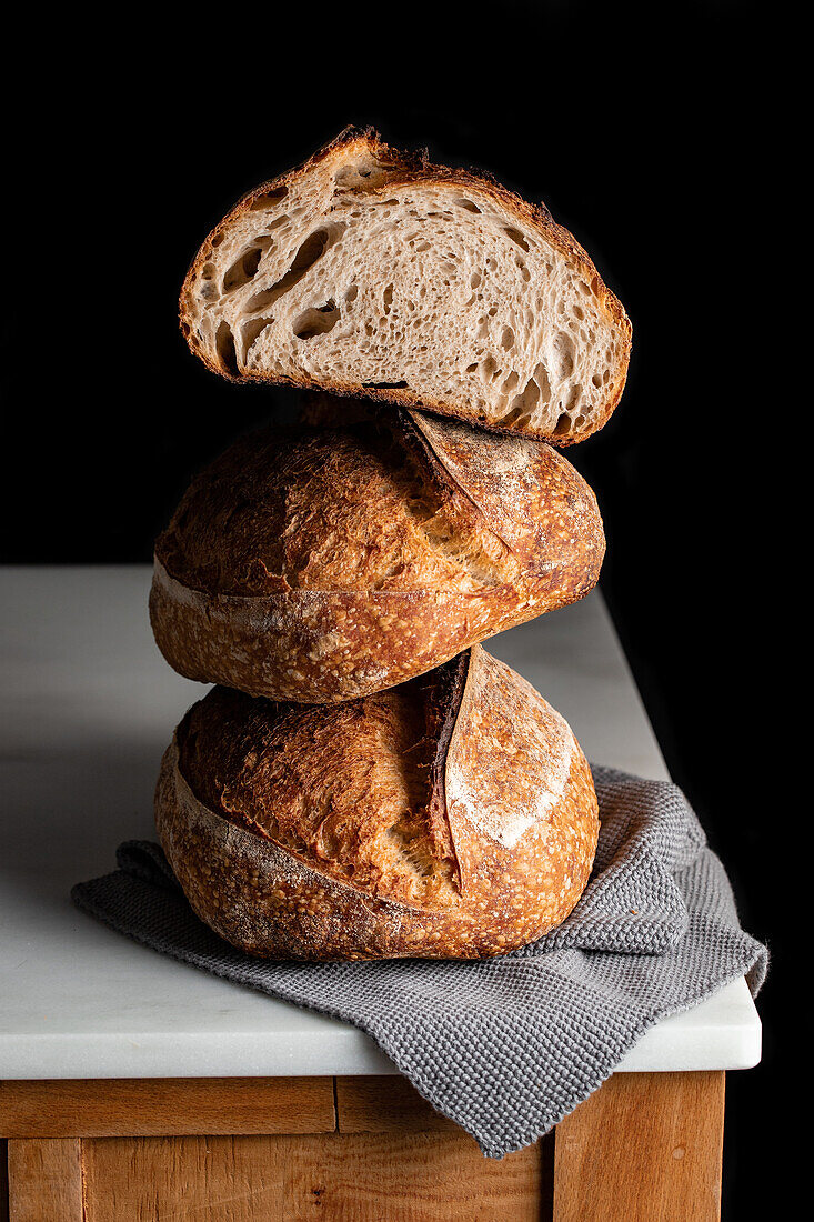 Tasty sourdough bread with brown crust placed on marble table against black backdrop