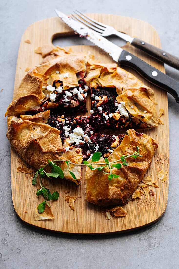 Top view of baked cut pie with beetroot and feta cheese on wooden cutting board with knife on gray background in kitchen