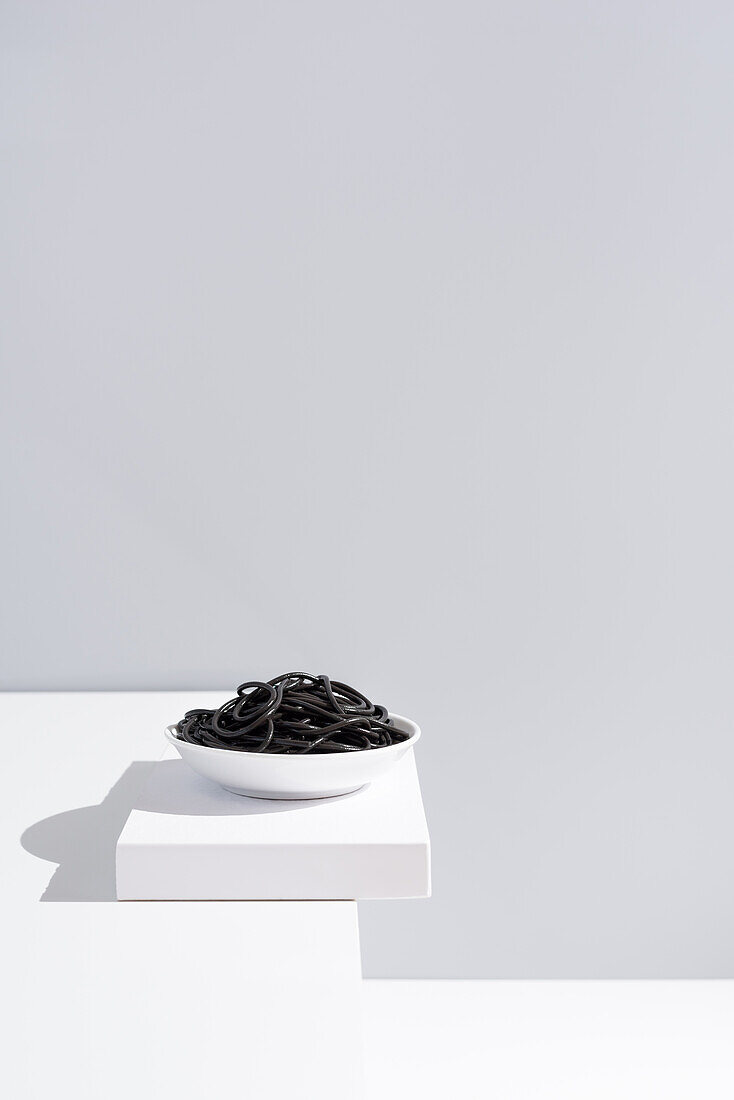 Minimalist studio with black squid ink spaghetti in full ceramic bowl on white table