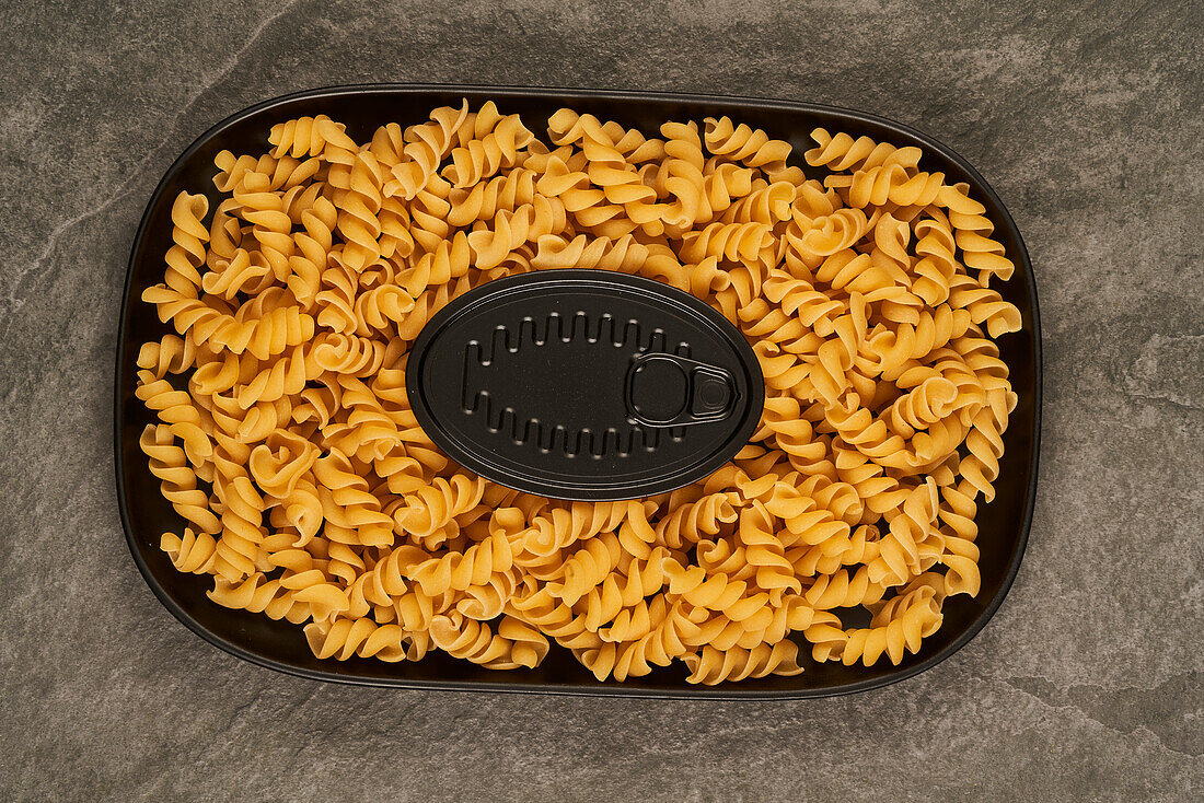 Schwarze Dose von oben neben ungekochten Fusilli-Nudeln auf einem Tablett auf dem Tisch