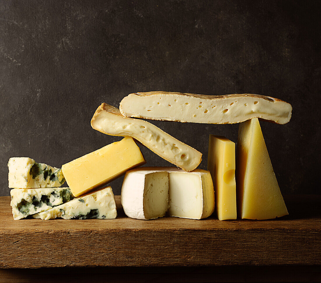 Various cut cheese on wooden board placed on wooden table