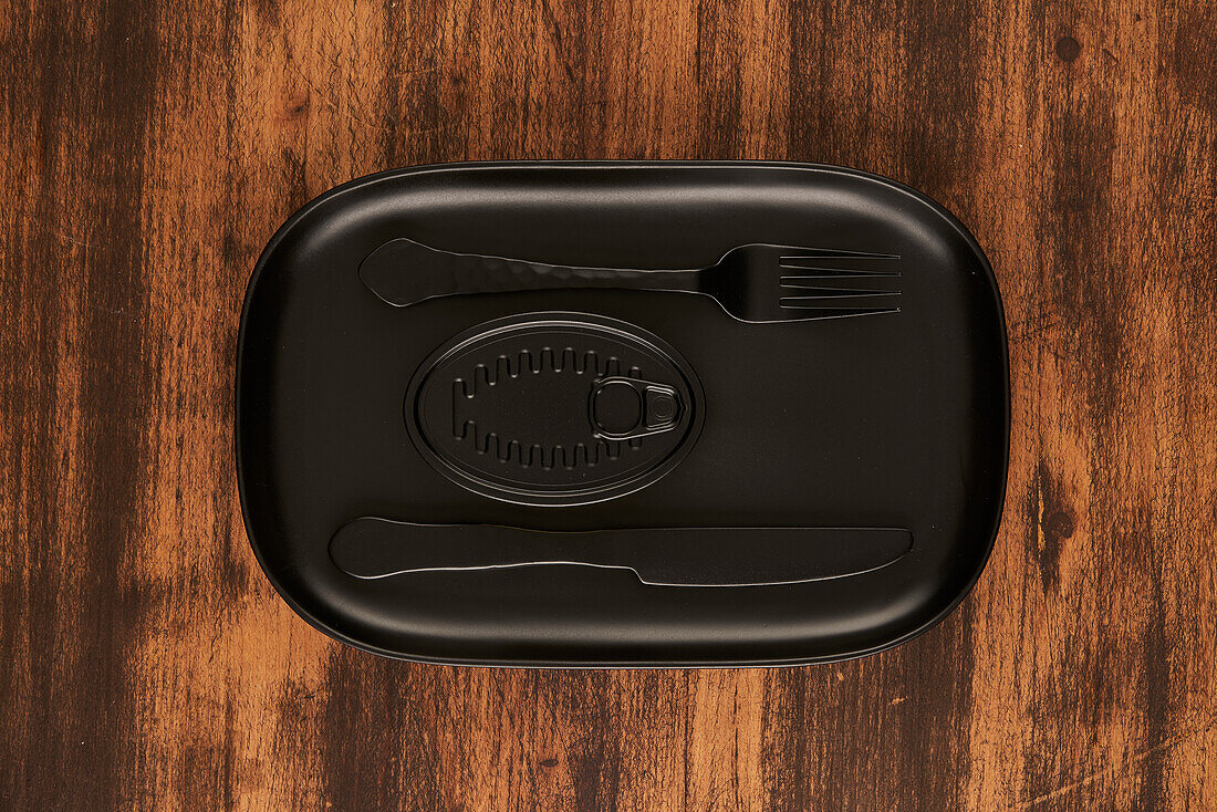 Top view of black fork and knife placed near sealed canned food on rectangular black tray