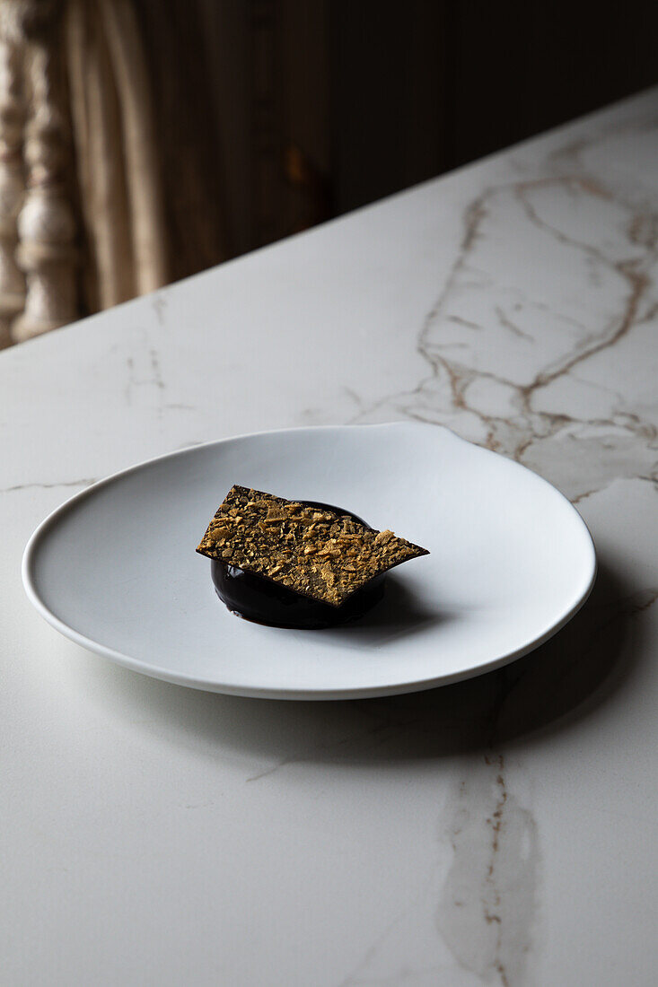 From above of delicious chocolate mousse dome cake served with crunch caramel on white plate placed on marble table