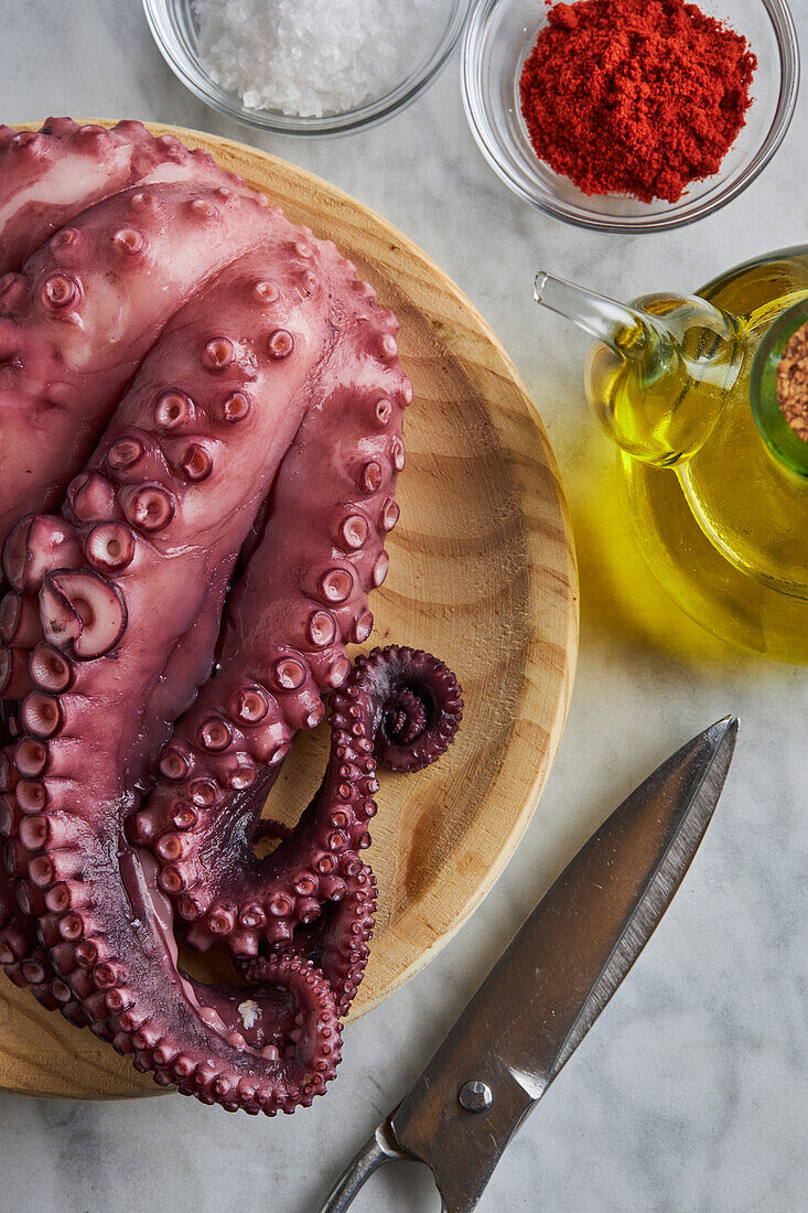 From above of fresh raw octopus placed on round wooden plate near metal scissors spices and oil