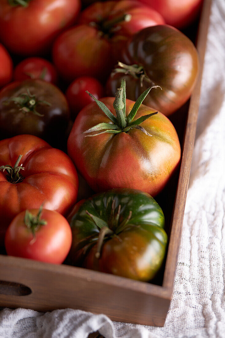 Draufsicht auf frische reife rote Tomaten in einer Holzkiste auf einer Leinenserviette auf dem Tisch