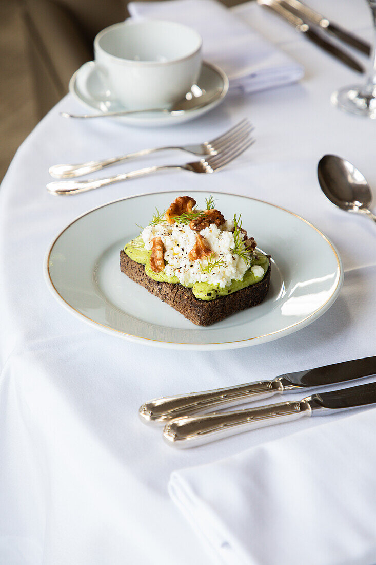 From above of healthy avocado toast with ricotta and walnuts placed on white plate and served on table in cafe during breakfast