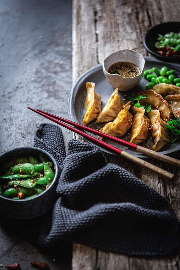 Gyozas mit grünen Bohnen und Sojasauce mit Sesam werden mit Stäbchen neben Schalen mit Gewürzen und Erbsenschoten platziert