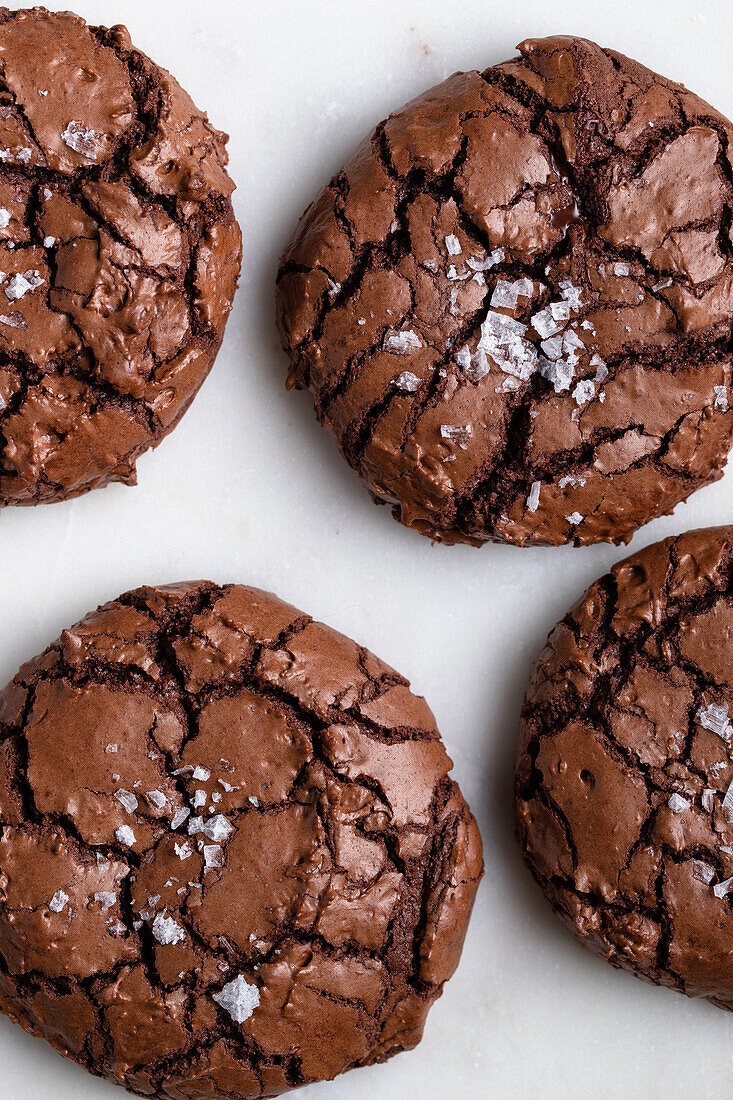Draufsicht auf süße, frisch gebackene Schokoladen-Brownie-Kekse mit Rissen auf weißem Hintergrund in einer hellen Küche zu Hause