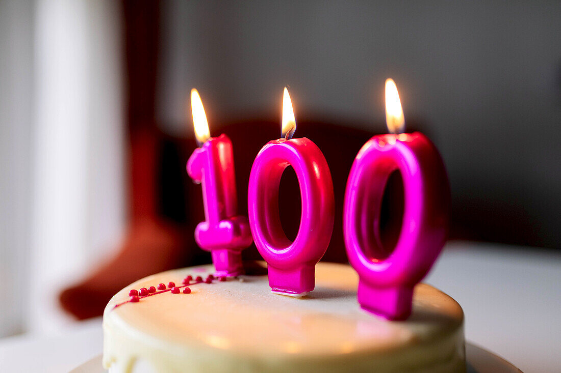 Brennende Kerzen mit der Zahl 100 auf einem süßen Geburtstagskuchen, der zum Feiern vorbereitet und auf den Tisch gestellt wurde