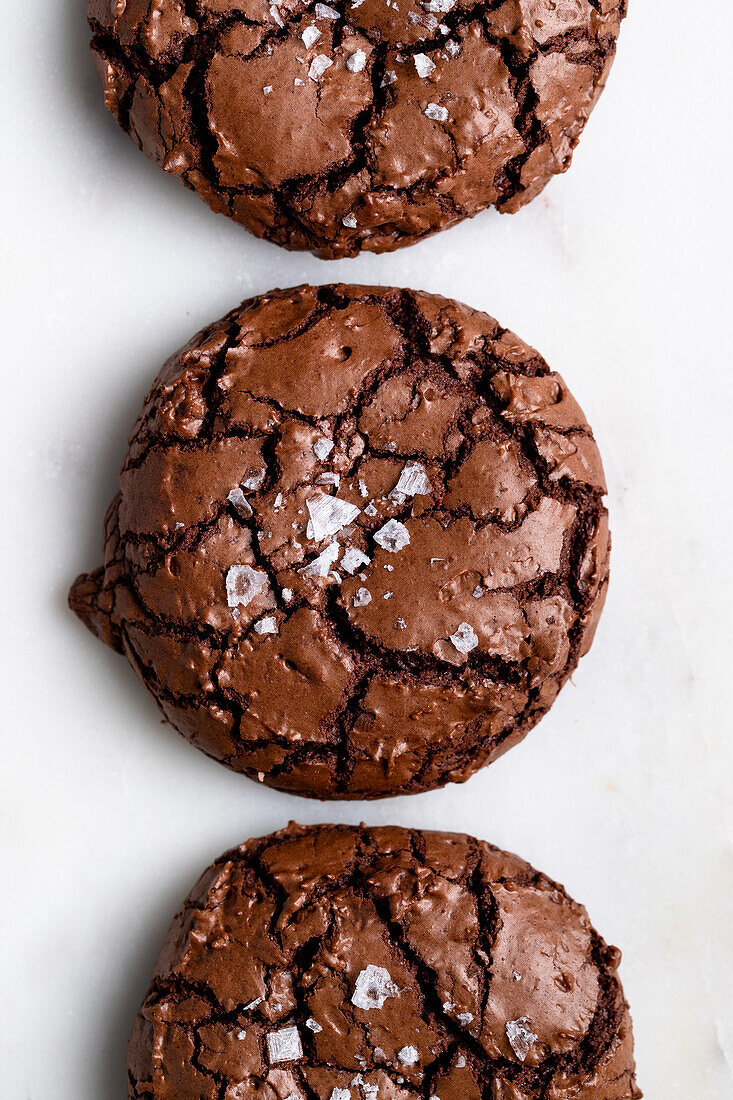 Draufsicht auf süße, frisch gebackene Schokoladen-Brownie-Kekse mit Rissen auf weißem Hintergrund in einer hellen Küche zu Hause